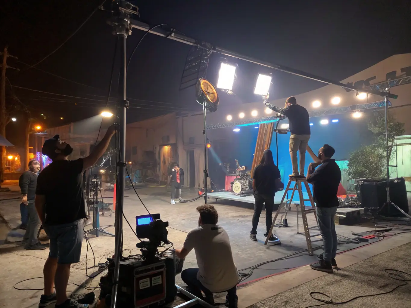 A behind-the-scenes shot of a music video shoot, showing a director giving instructions to the artist and crew, with professional lighting and camera equipment visible.